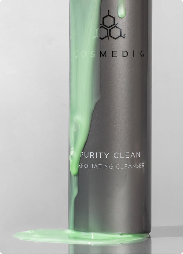 Close up of bottom half of Purity Clean Exfoliating Cleanser with green cleanser dripping against light gray background.
