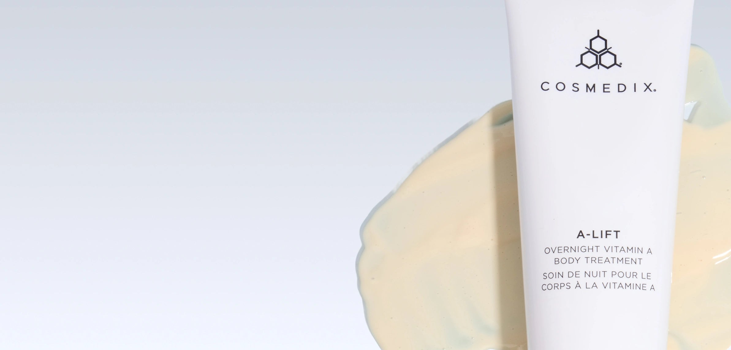 Cosmedix A-Lift Overnight Vitamin A Body Treatment product display featuring the brand logo and name at the top right, with a generous dollop of creamy yellow product shown on the left side against a light blue-gray background. Product description text and bilingual labeling (English and French) appear on the right side. A small blue dot marks the product application point.