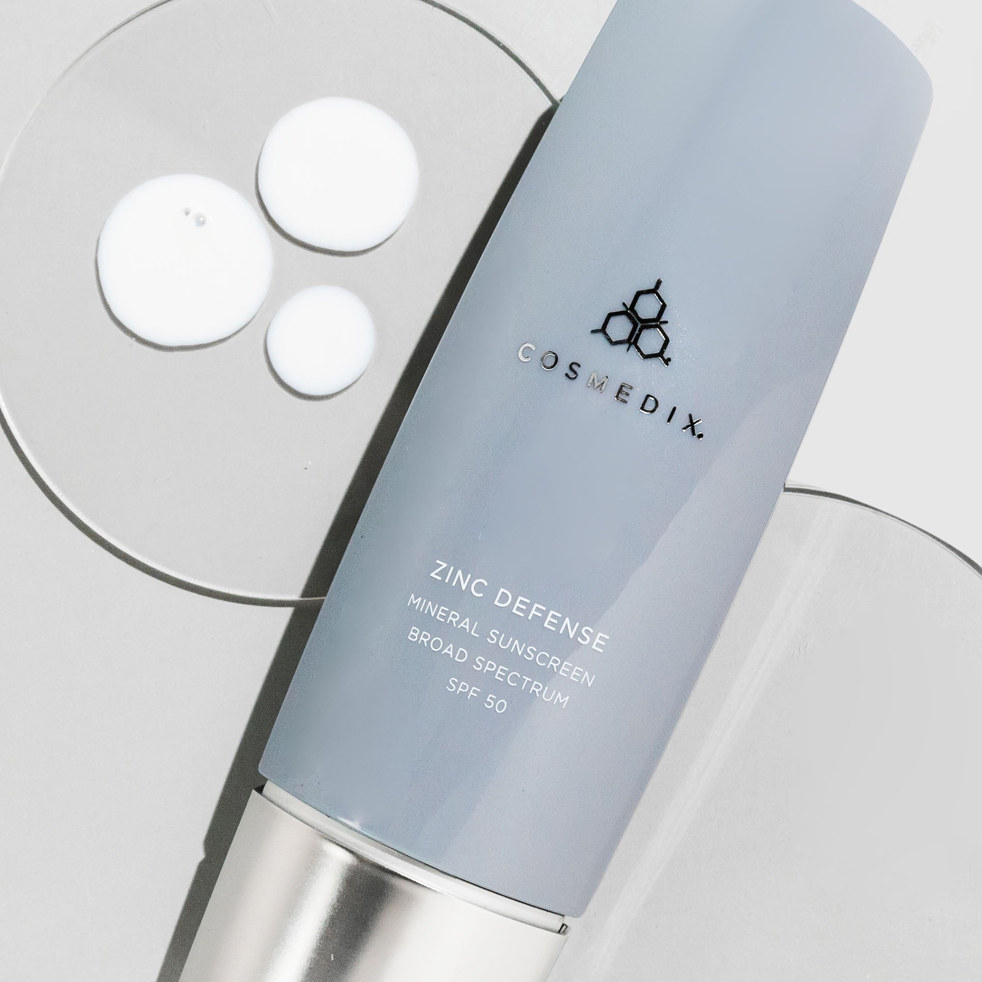 CosMedix Zinc Defense sunscreen box with white circular samples on a light surface.